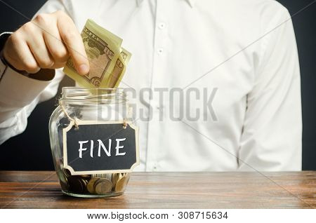A Man Puts Dollars In A Glass Jar With The Word Fine. Saving Money And Paying A Fine. Punishment For