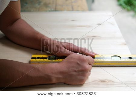 Carpenter Marking Straight Line On Plywood Sheet Using Spirit Level In Carpentry Workshop. Measuring
