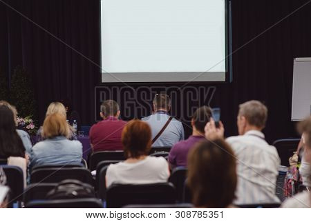 A Big White Screen Without Text. A Conference Concept. People Sitting And Watching Blank Screen For 
