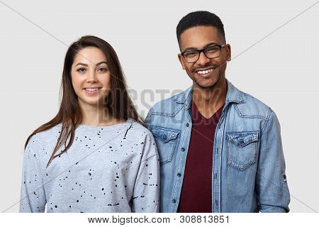 Horizontal Shot Of Happy Dark Skinned Young Man And European Woman, Standing With Positive Expressio