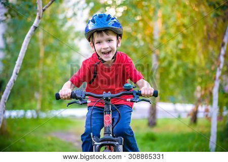 A Small White Toddler Boy In A Protective Helmet On His Head Sits On A Children's Bicycle. Toddler O
