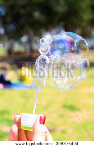Female Hand Holding A Wand For Triggering Soap Bubbles On Green Background