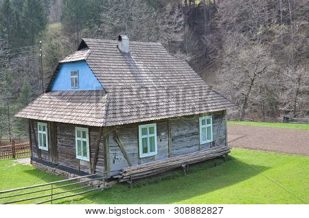 Wooden House In The Mountains On A Hill, Fenced By A Wooden Fence, In Early Spring Surrounded By Tre