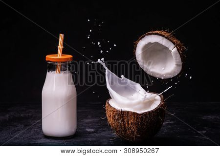 Coconut Milk Splash In The Middle Of The Fresh Coconut, And Coconut Milk In The Bottle. Dark Backgro