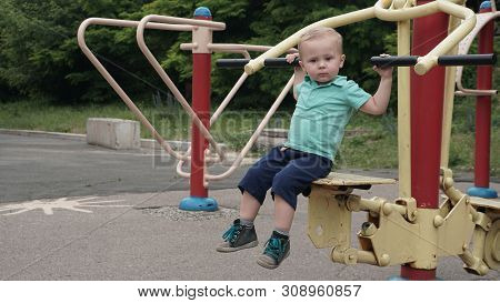 Cute Child Sitting On The Training Apparatus Ang Holding Handles In A Sportground