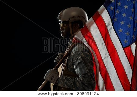 Side View Of American Ranker With Armour Confidently Standing With Weapon And Flag On Shoulder, Look