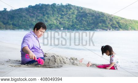 Family Traveled To The Beach On Vacation. Father And Daughter Lounge In The Sand By Beach. During In