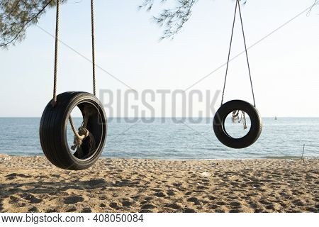 Tire Swings Hang From Trees On The Sandy Beach. With A Background Of Blue Sea And Sky With Coluds