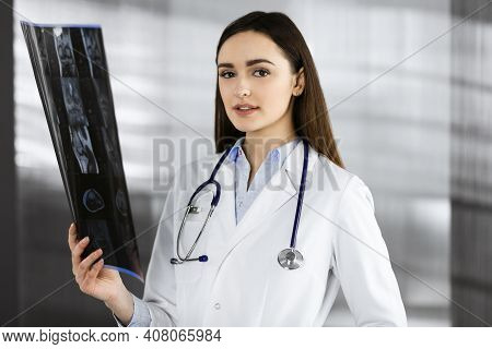 Professional Young Woman-doctor Is Looking At Her Patients Roentgenogram. Physician At Work In A Cli