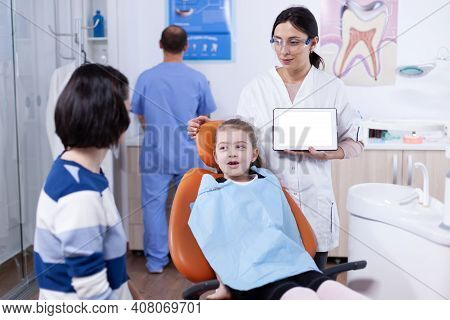 Little Girl Sitting In Dental Chair And Pediatric Dentist Using Tablet Pc With Chroma Key. Stomatolo