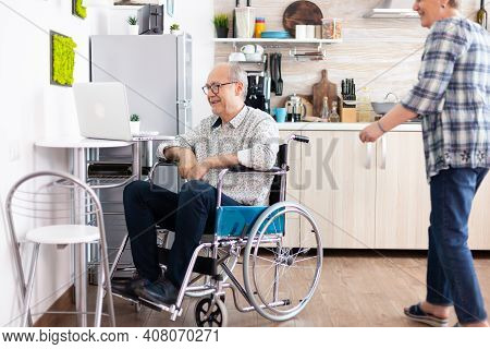 Senior Couple Laughing Using Laptop, Husband Calling His Wife Near Him During A Video Call With Gran
