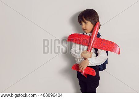 Boy Child In A White Shirt And Jeans Flies On A Red Airplane Toy At The White Wall Of The House