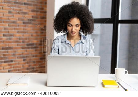Diligent Young American Businesswoman Sitting At The Laptop, Typing A New Work Strategy, Creating A 