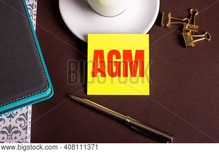 Agm Annual General Meeting Written On Yellow Paper On A Brown Background Near A Coffee Cup And Diari