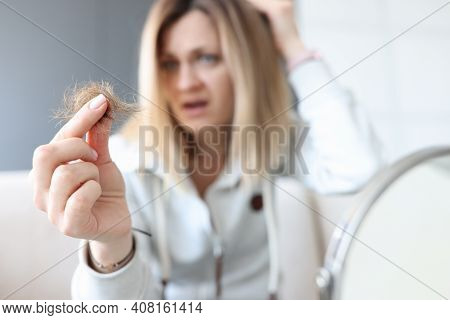 Frustrated Woman Holds Bun Of Her Hair In Her Hand. Hair Loss Concept