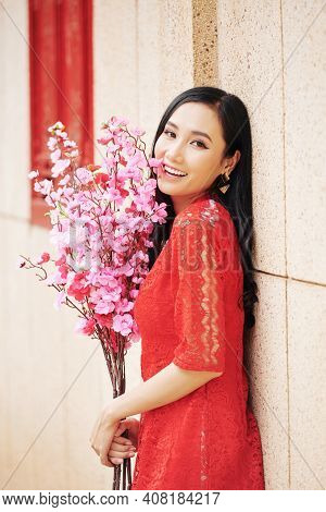 Happy Beautiful Young Vietnamese Woman In Red Dress Standing Outdoors With Brahches Of Pink Peach Bl