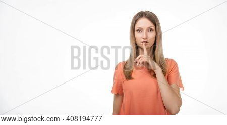 Portrait Of Young Blond Woman Keeping Finger At Her Mouth, Saying Shh, Hush, Tsss. Silence And Secre