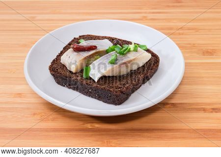 Open Sandwich Made Of Brown Bread, Slices Of Fillet Of Pickled Atlantic Herring And Chopped Green On
