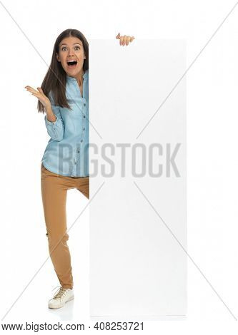 young casual woman feeling happily surprised and holding a billboard against white background