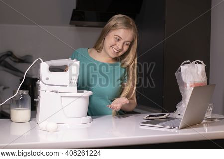 A Blonde Woman Videoblogger Cooking In Modern Kitchen Near Laptop, Online Learning Or Remote Cooking