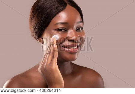 Closeup Portrait Of Beautiful Nude Black Woman Applying Moisturising Cream On Face, Attractive Afric