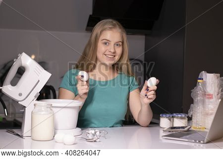 A Blonde Woman Videoblogger Cooking In Modern Kitchen Near Laptop, Online Learning Or Remote Cooking