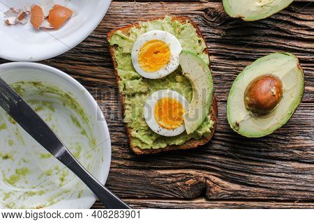 Toast with mashed avocado and eggs on messy rustic wooden table from above