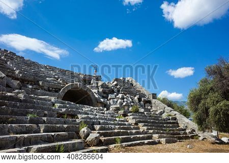 Rows of stone seats of ruins of Theatre in Letoon Ancient City in village Kumluova, Turkey. Sunny day, Tourist stands at top of amphitheater with hands up, Greek culture architecture