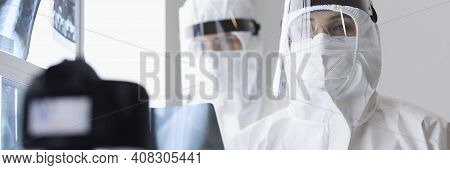 Doctors In Protective Screens And Anti-plague Suits Looking Into Camera In X-ray Room. Blogging Duri