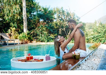 Fresh And Cool Asian Food On Floating Table In Swimming Pool. Loving Guy And Girl Hug Each Other Aro