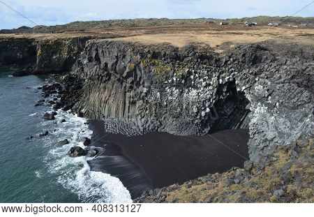 Towering Basalt Column Cliffs And Black Sand Beach On The Coast Of Iceland.