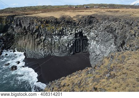 Tall Cliffs Made Of Rock Basalt Columns And A Black Sand Beach.