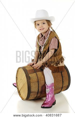 En glad førskole cowgirl skrævende et rustikt træ tønde, som om det var en hest.  På en hvid baggrund