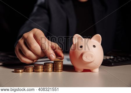 Businessman Calculates Profit, Piggy Bank With Stack Of Coins At The Desk. Savings And Investment Co
