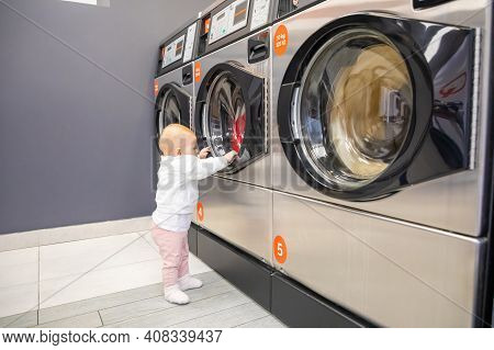 Prague, Czech Republic - 16.12.2020: Baby Girl Waiting For Laundry In Laundry Room With Speed Queen 