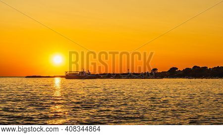 Amazing Sunset With Defined Sun And Reflection On Water. Silhouettes Of Boats And Cruise Ship Moored