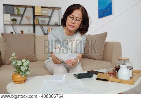 Pensive Elegant Senior Woman In Glasses Checking Bills And Calusing Expenses When Drinking Tea In He