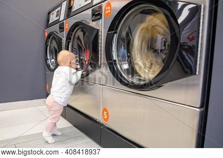 Prague, Czech Republic - 16.12.2020: Baby Girl Waiting For Laundry In Laundry Room With Speed Queen 