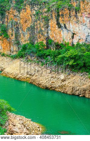 Lake With Natural Green Water Surrounded By Wall Of Sedimentary Rocks And On The Lake Shore, And The