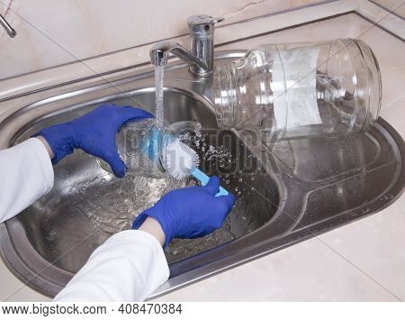 Woman's Hands With Gloves Washing Dish With Fresh Water At Kitchen Faucet Over The Metal Sink. Human