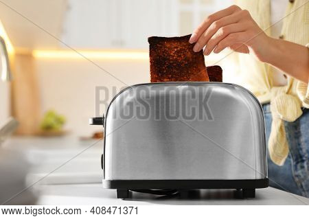 Woman Taking Slice Of Burnt Bread From Toaster In Kitchen, Closeup