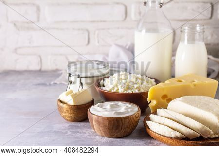 Various Fresh Dairy Products, Milk, Sour Cream, Cottage Cheese, Yogurt And Butter On A Light Stone C