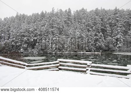 Snow On A Fence With Forest And River In Background On A Winter Day