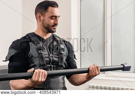 Portrait Of Young Sporty Man In Ems Suit Lifting Bar In Modern Gym