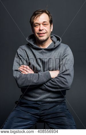 Studio Portrait Of A 40-50-year-old Smiling Man In A Gray Hoodie On A Neutral Background, Looking Di