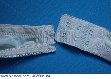 Two White Straps Made Of Fabric With Fasteners On The Bra Lies On A Blue Table