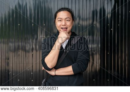 Asian Man Stands In Front Of Black Zince Background With The Confident Mood.