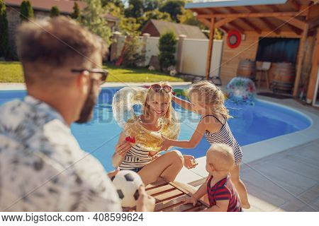 Parents Playing With Their Little Children By The Swimming Pool On A Hot Sunny Summer Day, Little Gi