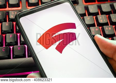 Red Stadia Logo On Mobile Phone Display With Color Gaming Keyboard In The Background. Game Platform 