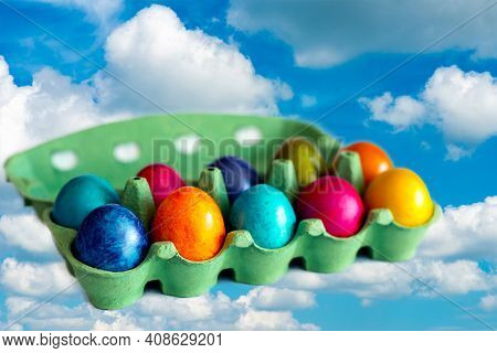 Colorful Eggs In The Open Carton Box On Blue Sky Background.eggs Flies Over Whites Clouds.
